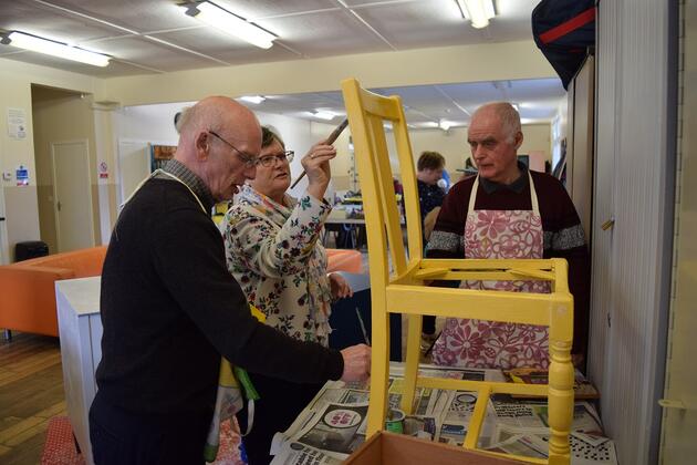 A group of three elderly participants paining a chair yellow